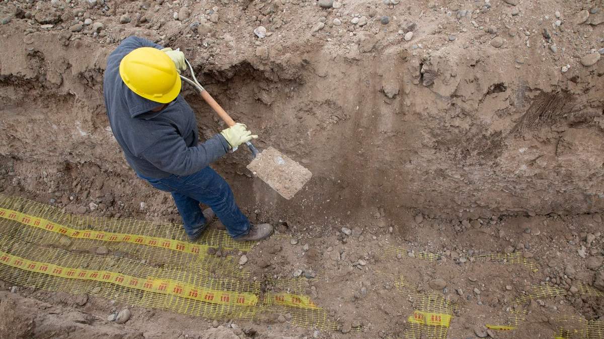 A worker excavating alongside a foundation to reach the footing