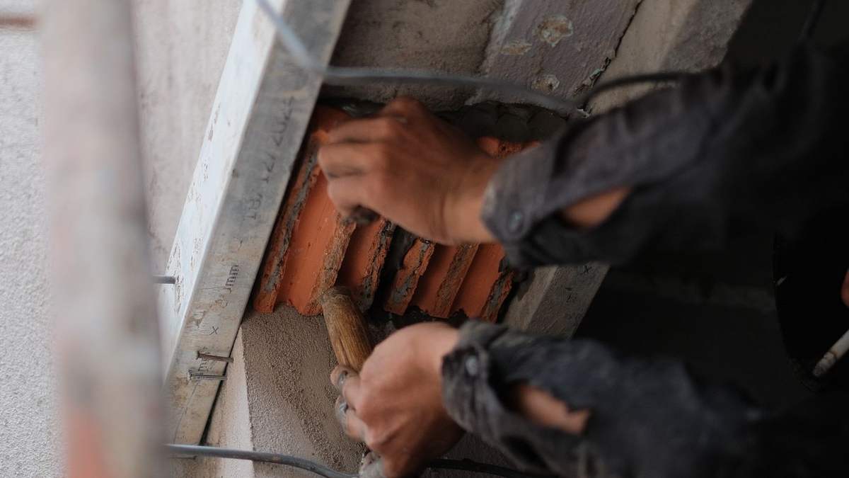 Hands repointing mortar in a cracked masonry wall with a trowel